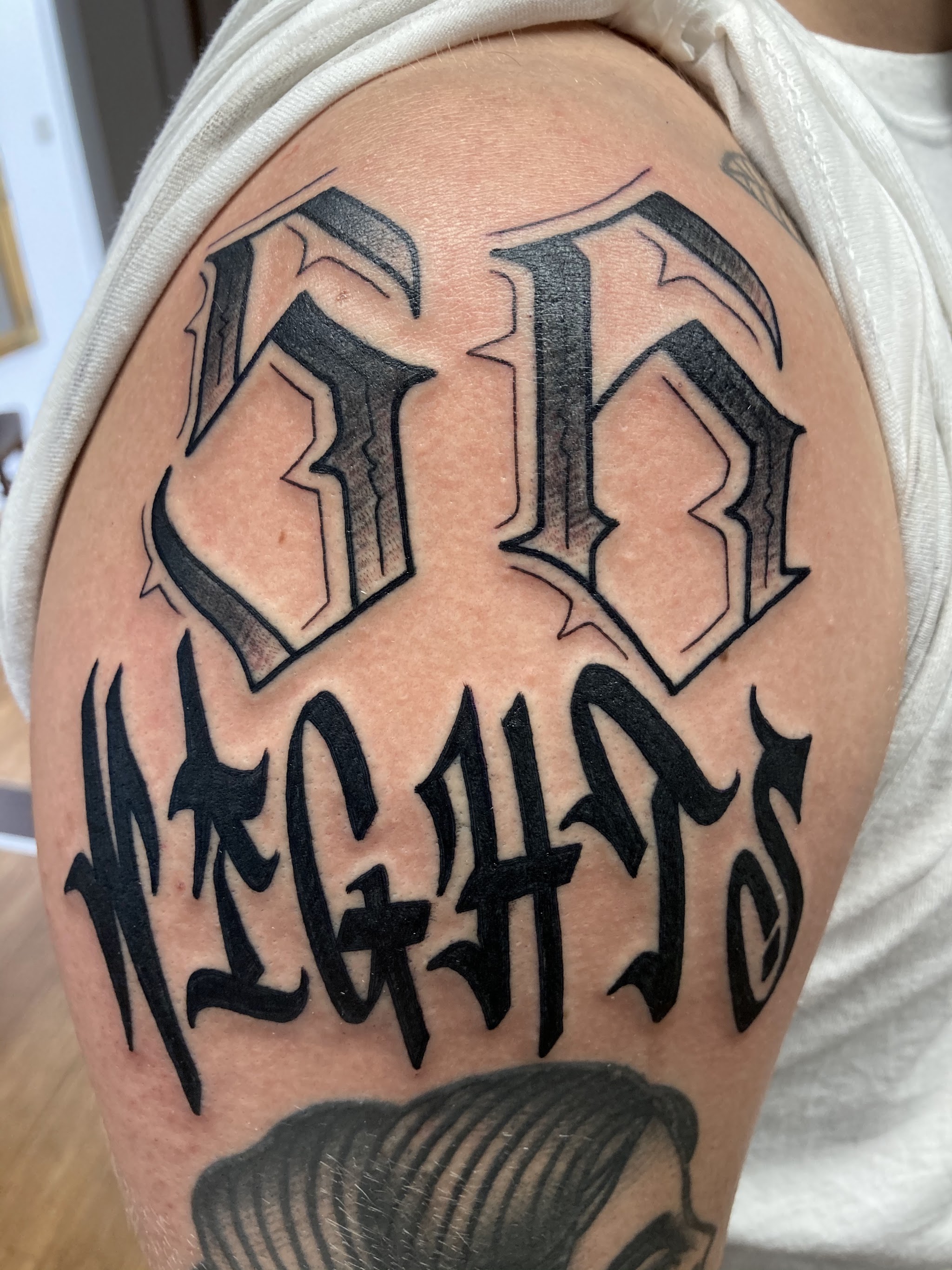 Blackletter-Lettering-Tattoo am Oberarm